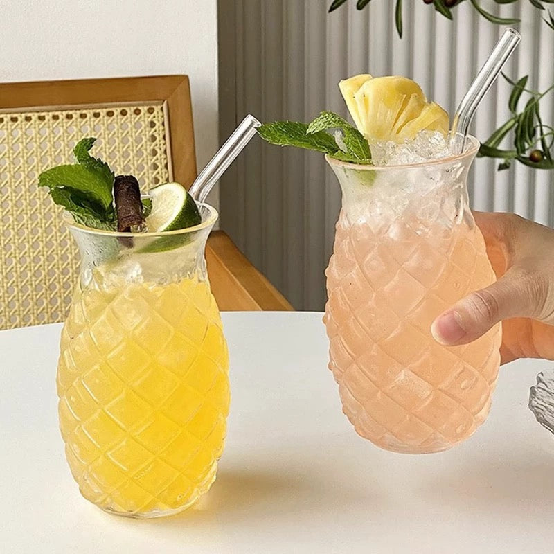 Two pineapple-themed glasses filled with drinks on a table.